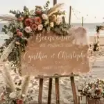 Panneau de bienvenue en plexi beige sur une plage avec une composition florale