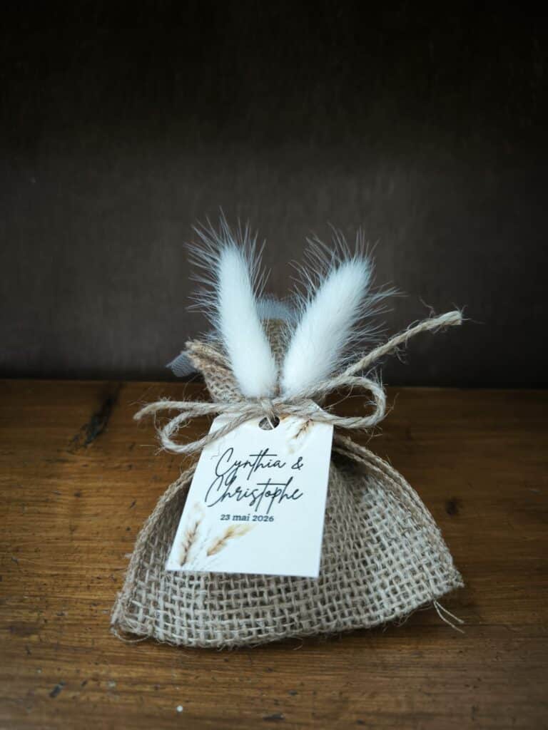 dragées de mariage personnalisés avec un sachet en toile de jute, des queues de lapin et une corde pour attacher une magnifique étiquette 100% personnalisée sur papier épais cartonné avec un visuel bohème. Le pochon est posé sur du bois