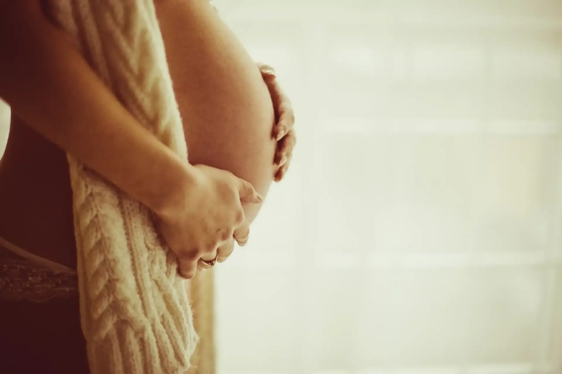 Femme enceinte qui pose ses mains sur le ventre nu, avec un tricot sur le coté du ventre