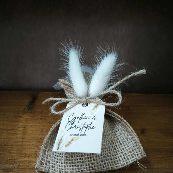 dragées de mariage personnalisés avec un sachet en toile de jute, des queues de lapin et une corde pour attacher une magnifique étiquette 100% personnalisée sur papier épais cartonné avec un visuel bohème. Le pochon est posé sur du bois